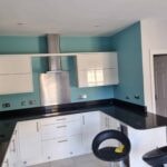 Kitchen with teal walls, white gloss units and a black worktop