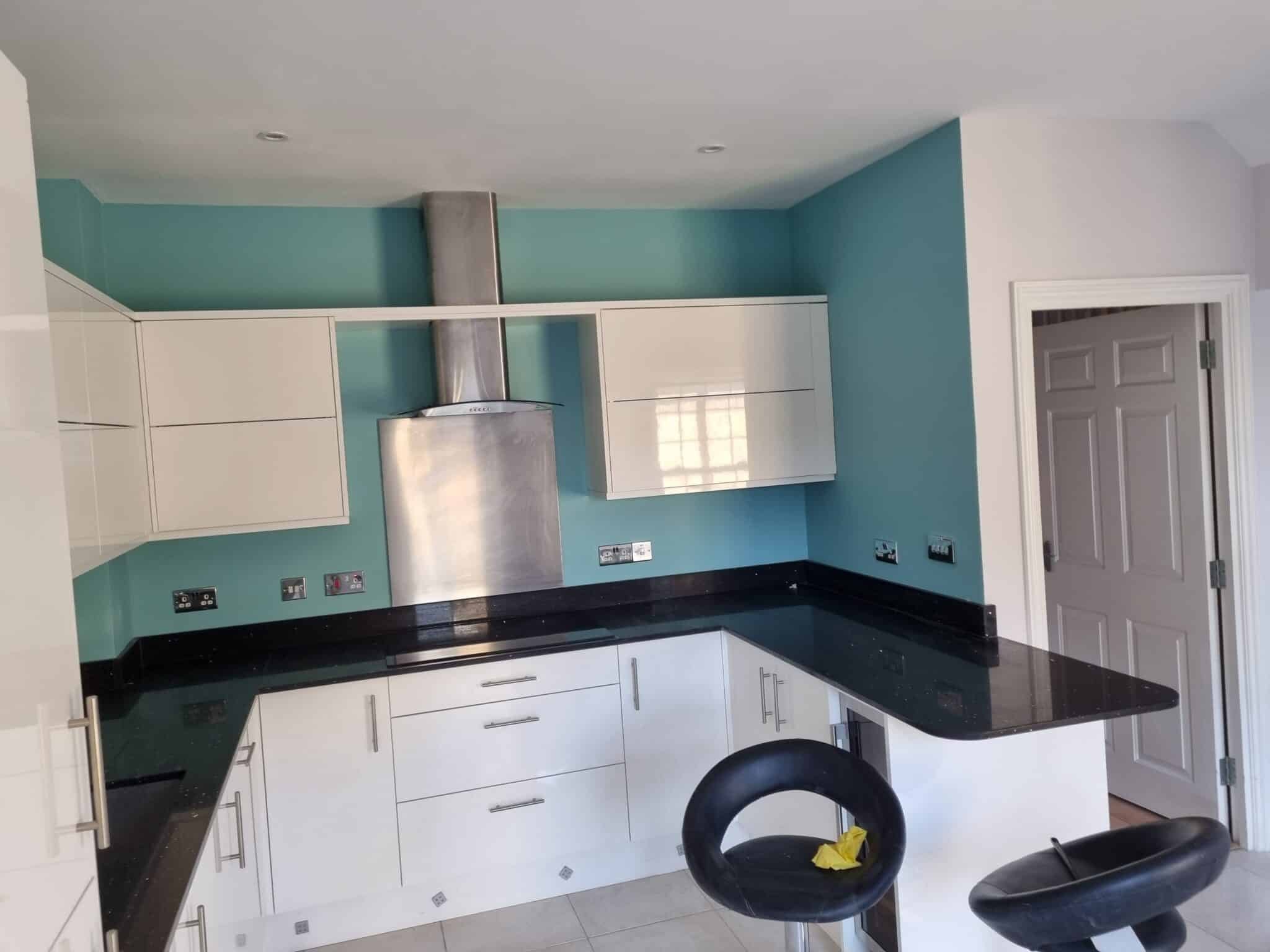 Kitchen with teal walls, white gloss units and a black worktop