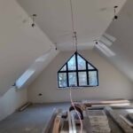 Loft room with sloping ceilings and an arched window, stripped back for work