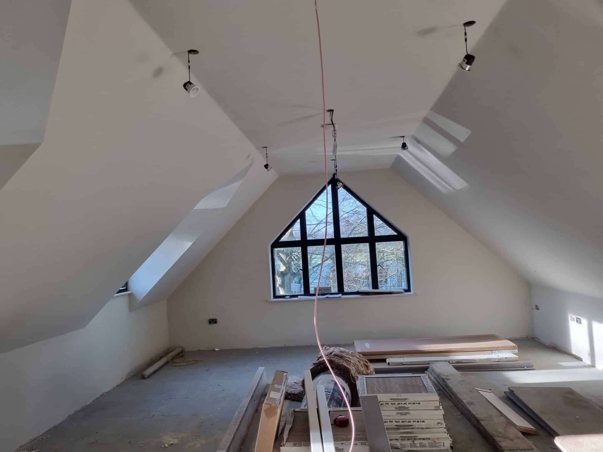 Loft room with sloping ceilings and an arched window, stripped back for work