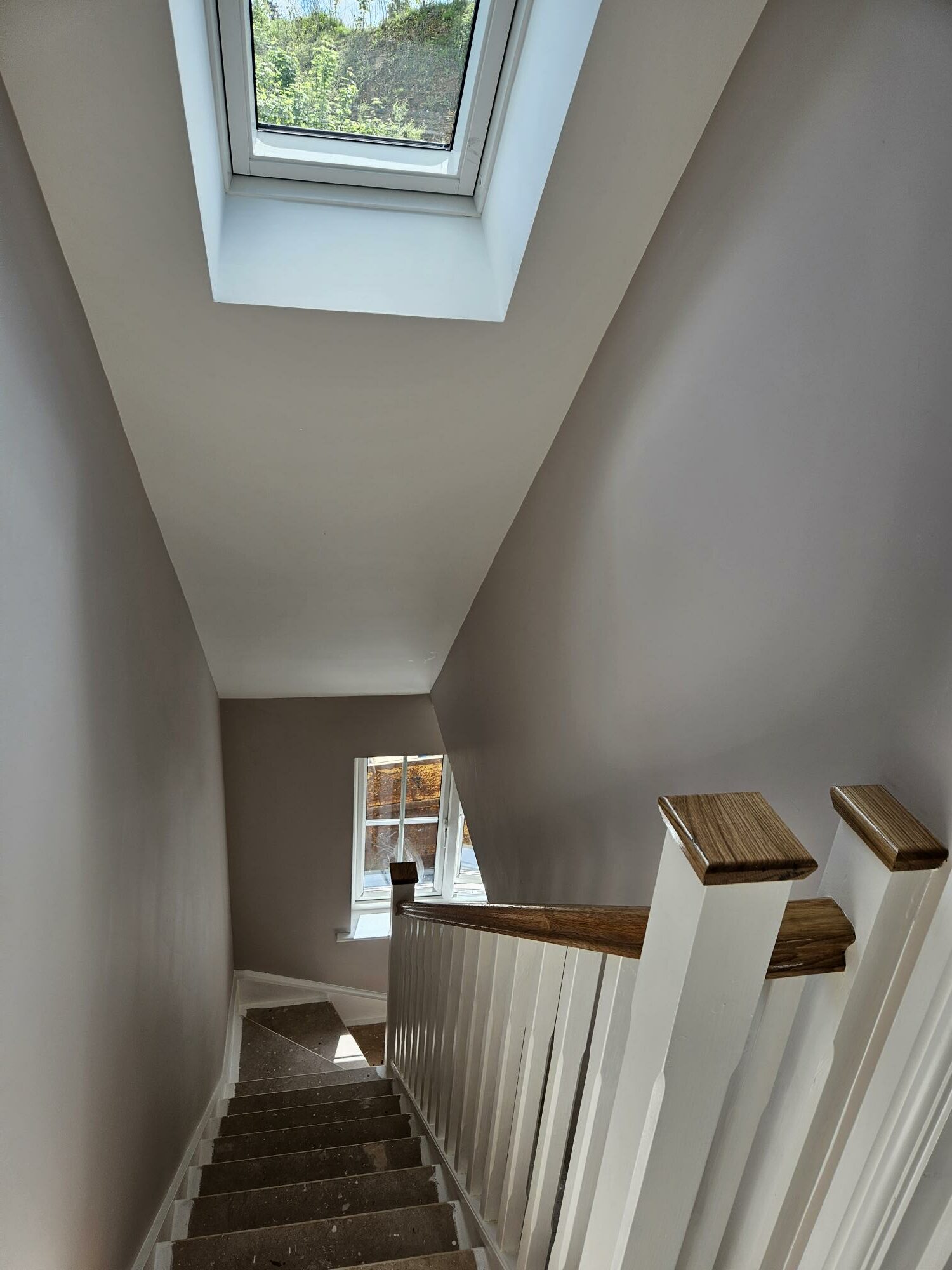 Stairwell with a roof window and white spindles with oak caps