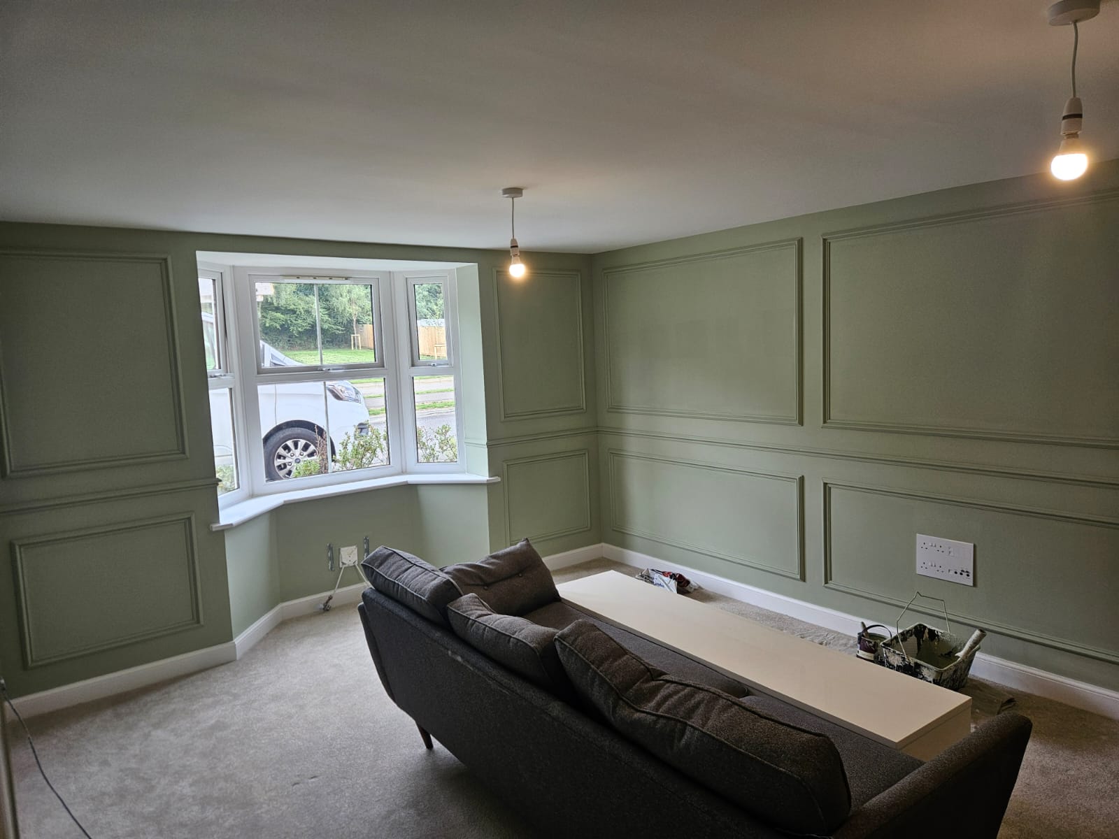 Sage green panelled living room with a bay window and a grey sofa