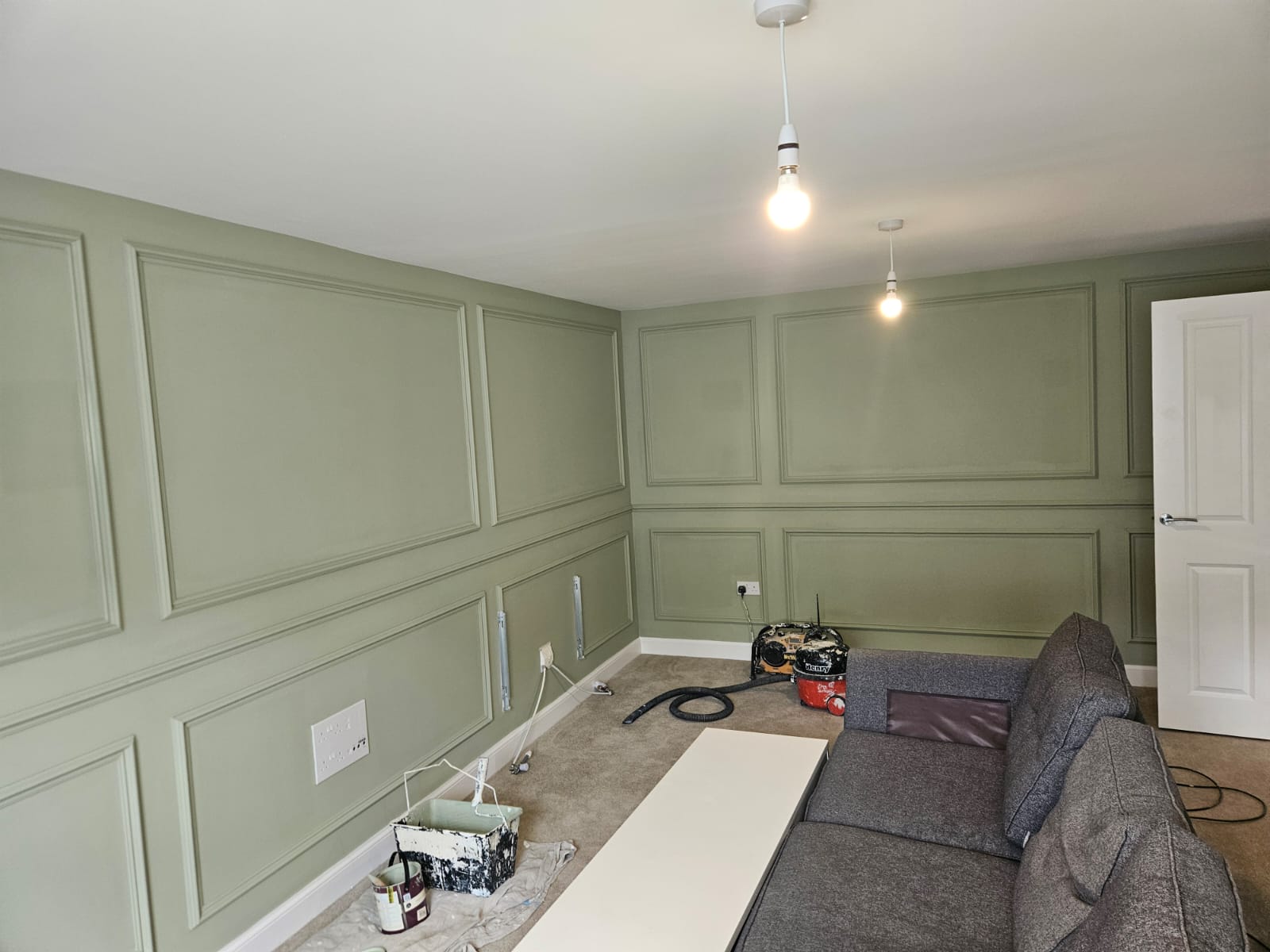 Living room with sage green panelled walls and a white ceiling